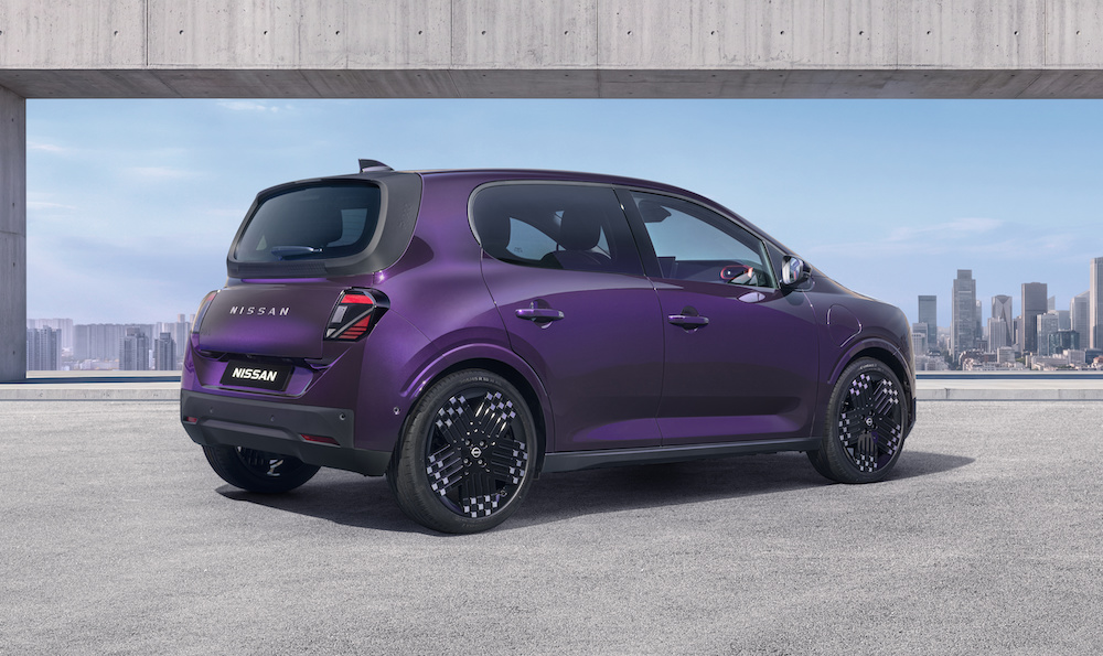 Three-quarter rear view of a purple Nissan PIXO electric city car parked beneath a modern concrete structure, with a city skyline in the background.