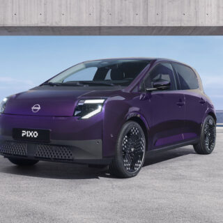 Three-quarter front view of a purple Nissan PIXO electric city car parked beneath a modern concrete structure, with a city skyline in the background.