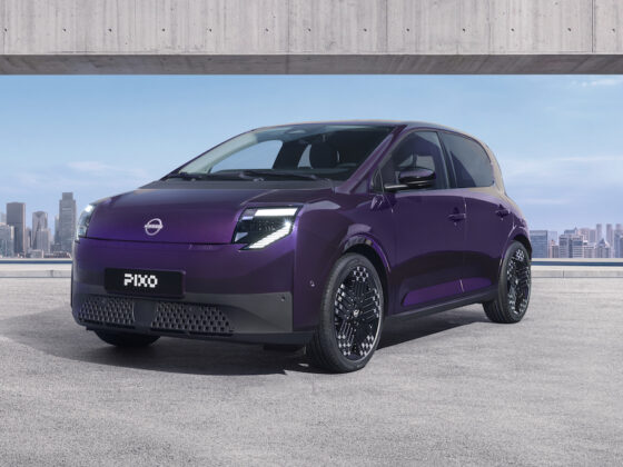 Three-quarter front view of a purple Nissan PIXO electric city car parked beneath a modern concrete structure, with a city skyline in the background.