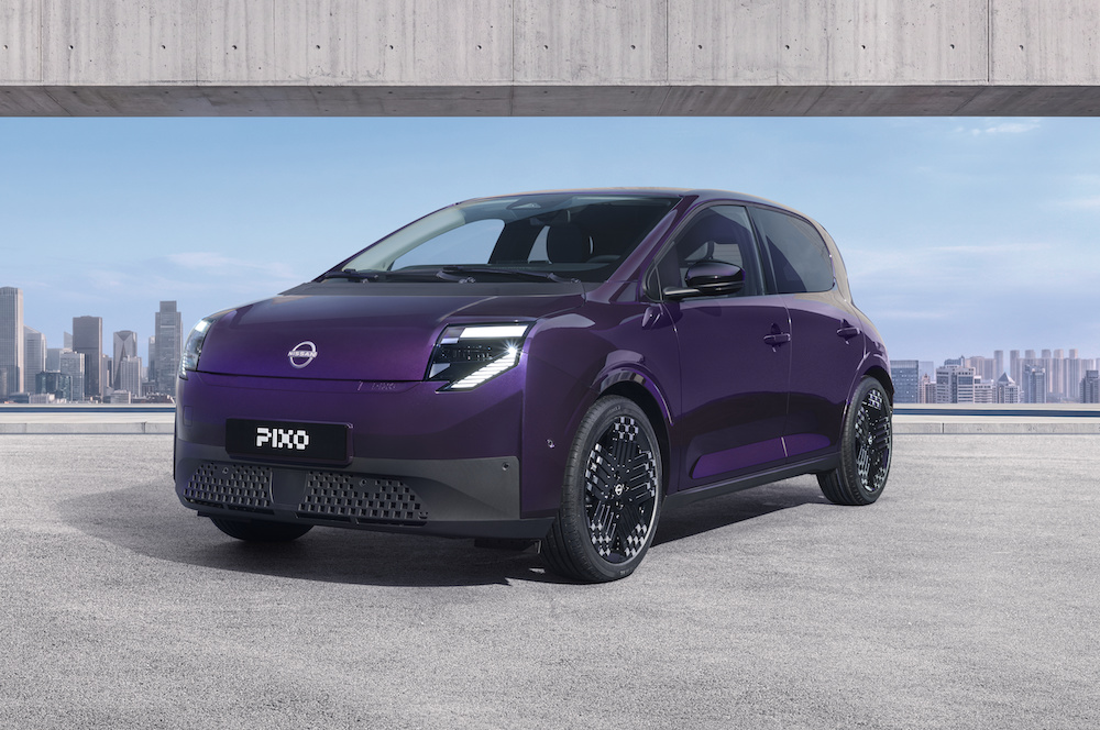 Three-quarter front view of a purple Nissan PIXO electric city car parked beneath a modern concrete structure, with a city skyline in the background.
